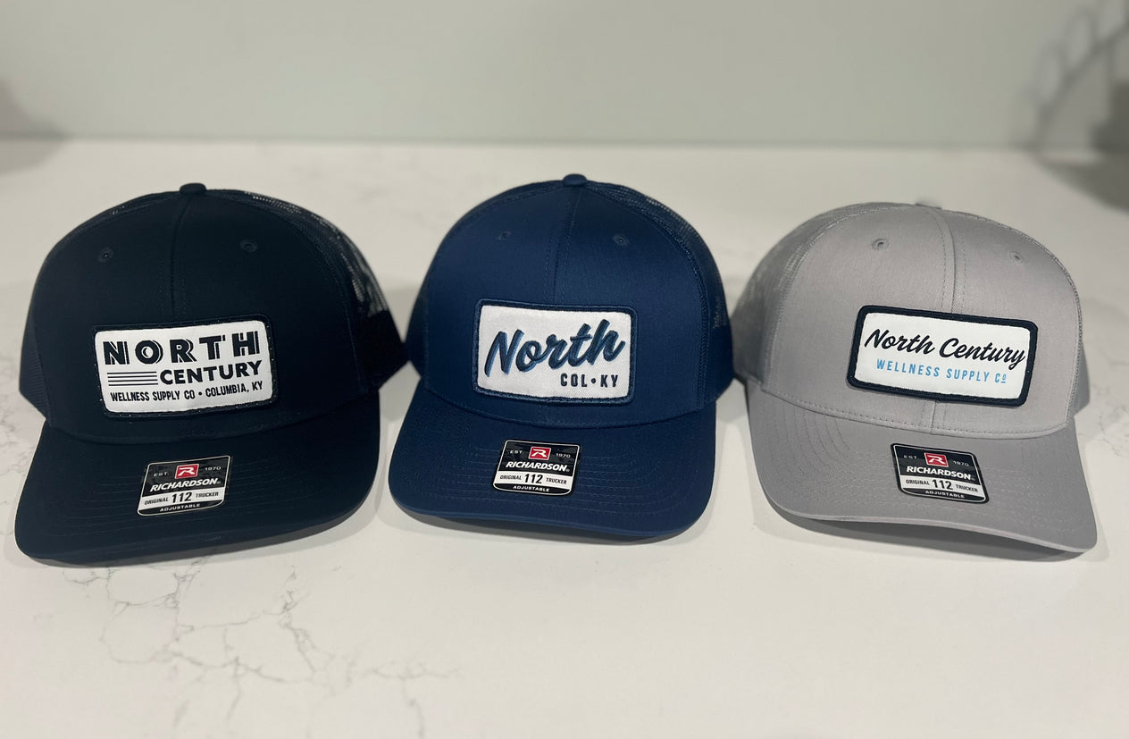 Three baseball caps in black, navy, and gray with 'North Century' branding on a white background.